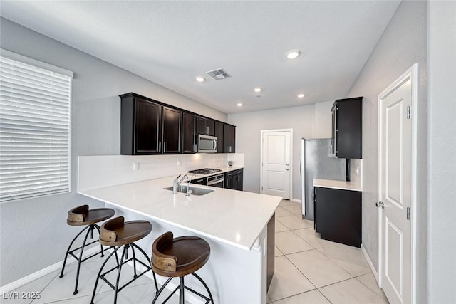 kitchen featuring visible vents, a breakfast bar, stainless steel appliances, a sink, and light tile patterned flooring