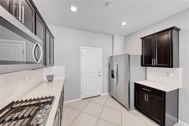 kitchen featuring light tile patterned floors, stainless steel appliances, light countertops, dark brown cabinets, and baseboards