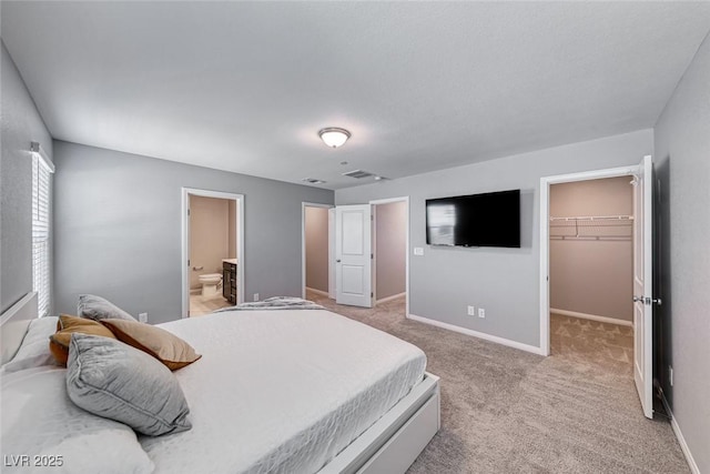 bedroom featuring baseboards, light colored carpet, ensuite bathroom, a spacious closet, and a closet