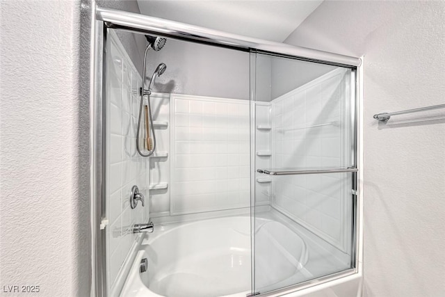 bathroom with a textured wall and combined bath / shower with glass door