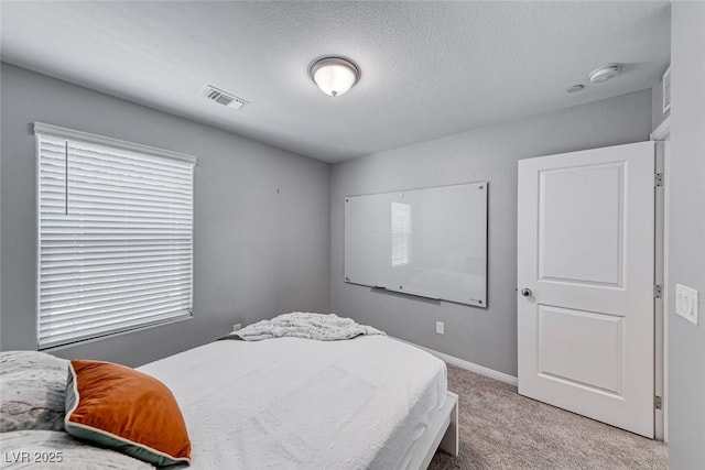 bedroom with visible vents, light carpet, a textured ceiling, and baseboards