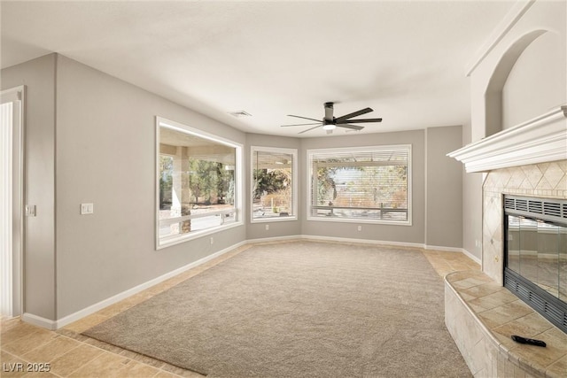unfurnished living room with light carpet, baseboards, ceiling fan, and a tile fireplace