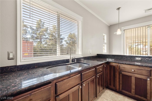 kitchen with a sink, dark stone countertops, visible vents, decorative light fixtures, and ornamental molding