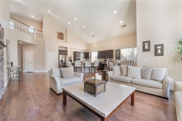 living room with recessed lighting, a high ceiling, wood finished floors, visible vents, and baseboards