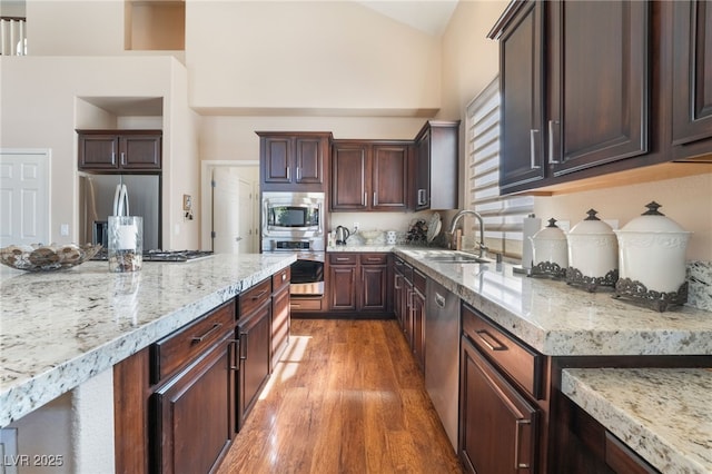 kitchen featuring stainless steel appliances, light stone counters, a sink, and light wood-style floors