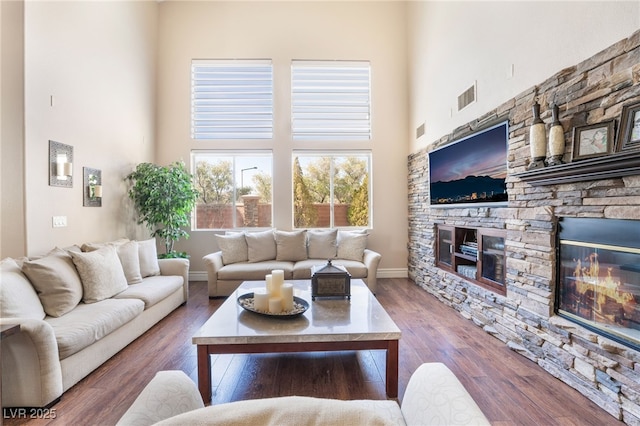 living room with a high ceiling, a fireplace, wood finished floors, and visible vents