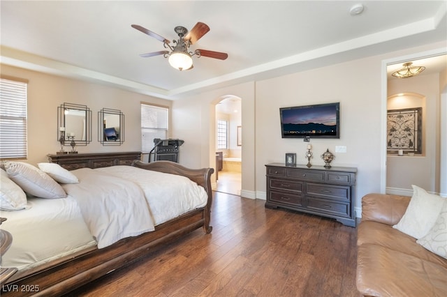 bedroom with arched walkways, a tray ceiling, multiple windows, and dark wood finished floors