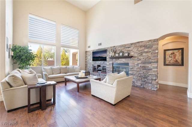 living room with a fireplace, visible vents, a high ceiling, wood finished floors, and baseboards