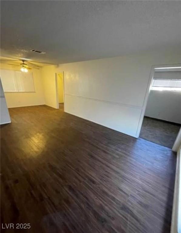 unfurnished living room with a ceiling fan, visible vents, and dark wood finished floors