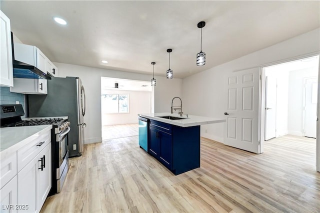 kitchen featuring light wood finished floors, appliances with stainless steel finishes, a kitchen island with sink, a sink, and blue cabinets