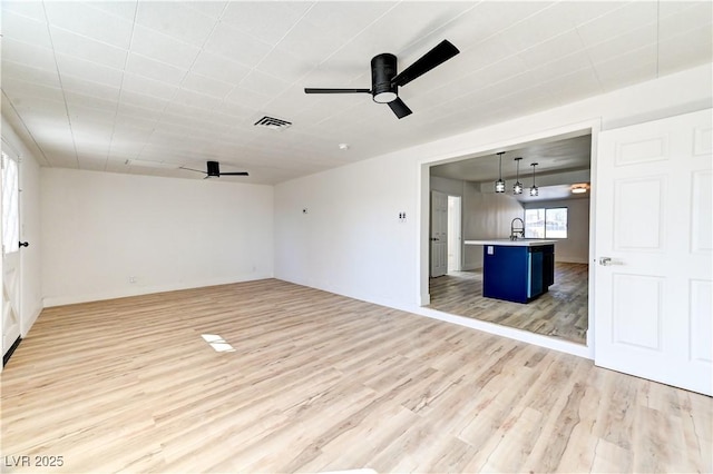 unfurnished living room with a ceiling fan, visible vents, a sink, and light wood-style flooring