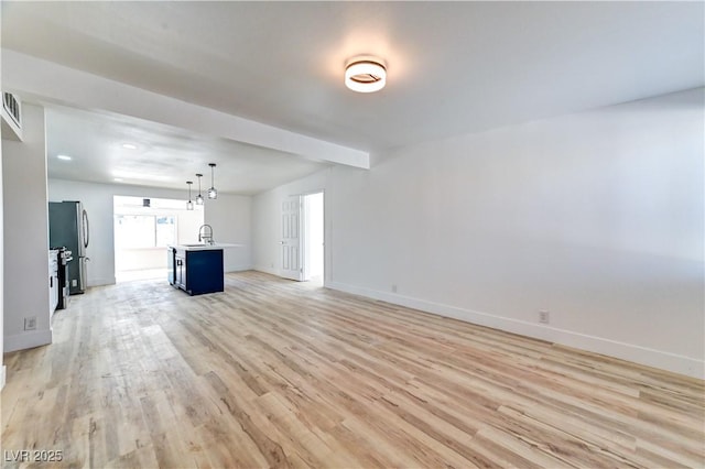 unfurnished living room featuring light wood-type flooring, visible vents, a sink, and baseboards