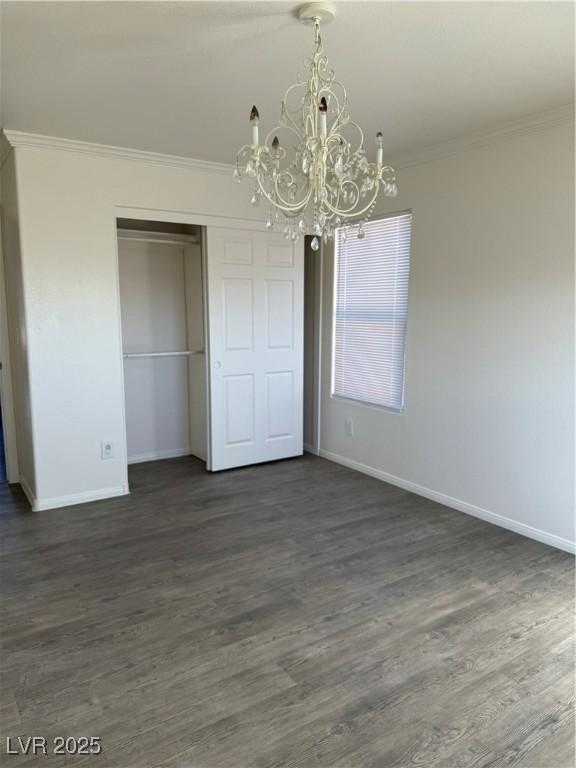 unfurnished dining area with baseboards, dark wood-style flooring, crown molding, and a chandelier