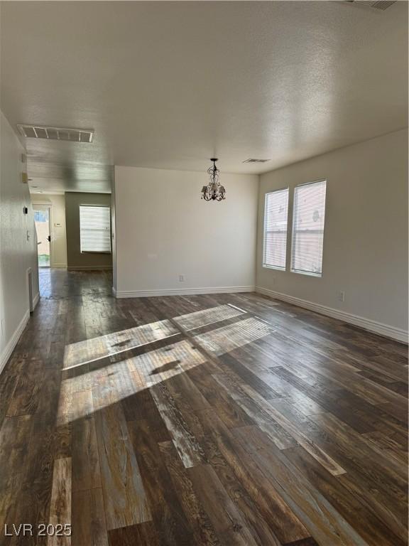 unfurnished room featuring dark wood-style floors, baseboards, visible vents, and a chandelier