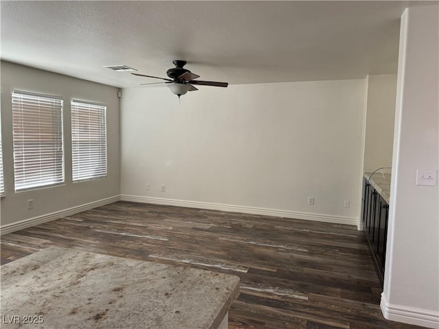 empty room with dark wood-type flooring, a ceiling fan, visible vents, and baseboards