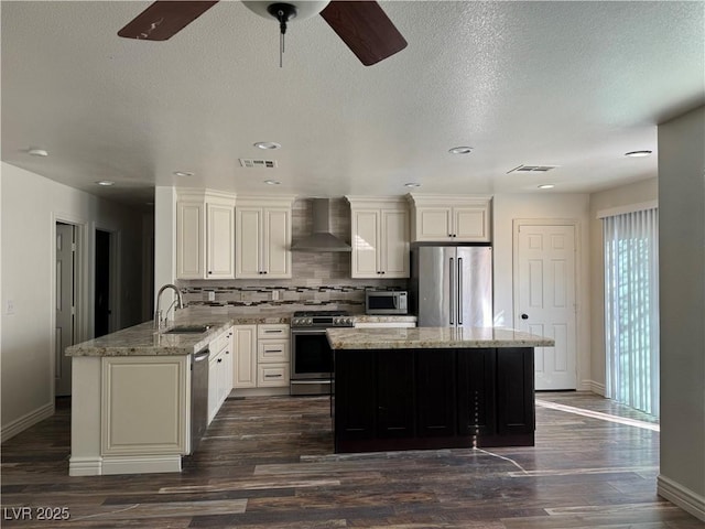 kitchen with stainless steel appliances, visible vents, a sink, wall chimney range hood, and a kitchen island