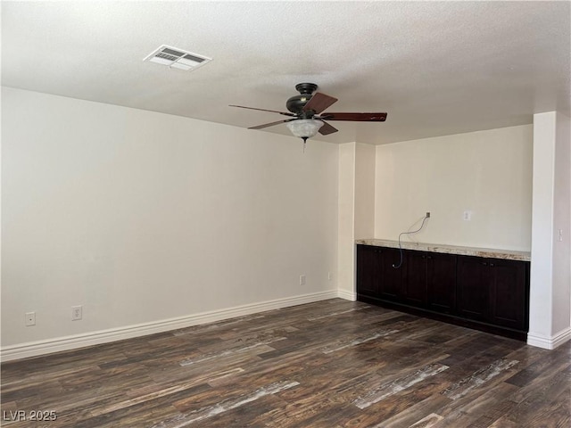 spare room featuring a textured ceiling, a ceiling fan, visible vents, baseboards, and dark wood-style floors