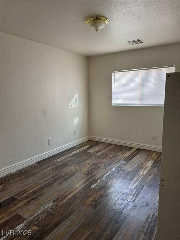 spare room with a textured ceiling, dark wood finished floors, visible vents, and baseboards