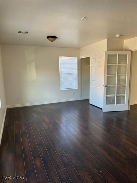 empty room featuring baseboards, visible vents, and dark wood finished floors