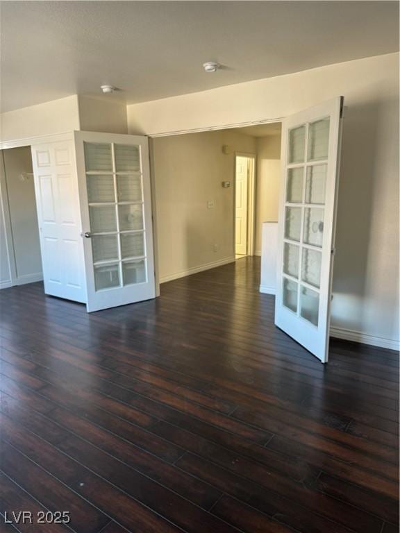 empty room featuring baseboards, dark wood-type flooring, and french doors