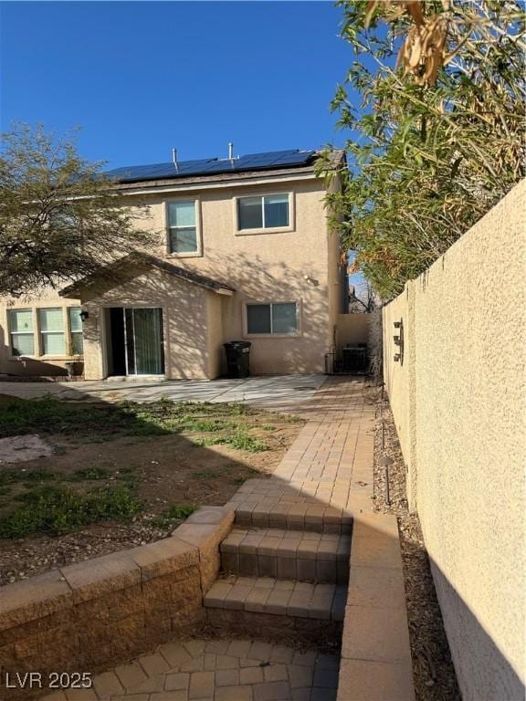 rear view of property featuring a patio, central AC unit, solar panels, fence, and stucco siding