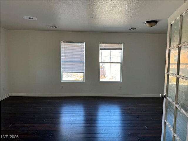 spare room featuring dark wood finished floors, visible vents, and baseboards