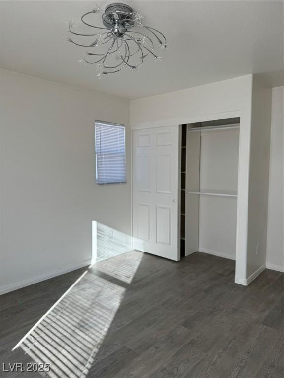 unfurnished bedroom with dark wood-style floors, a closet, and baseboards