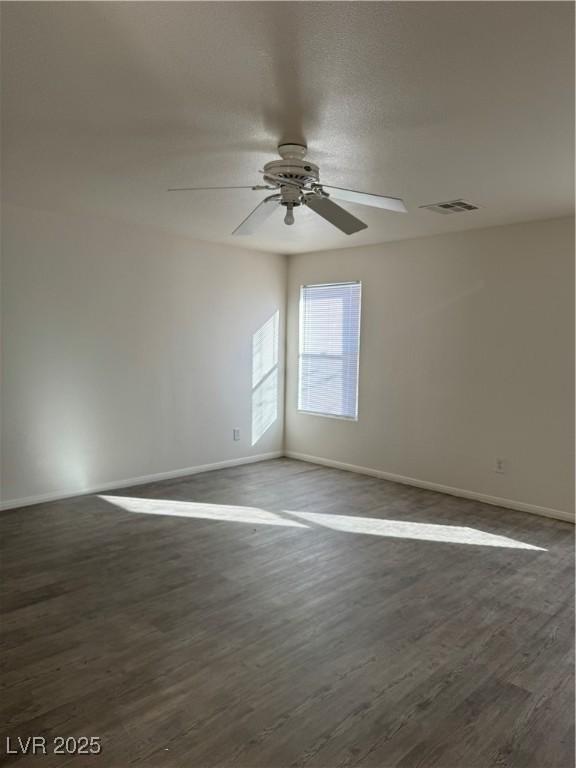 unfurnished room with dark wood-type flooring, visible vents, baseboards, and a ceiling fan