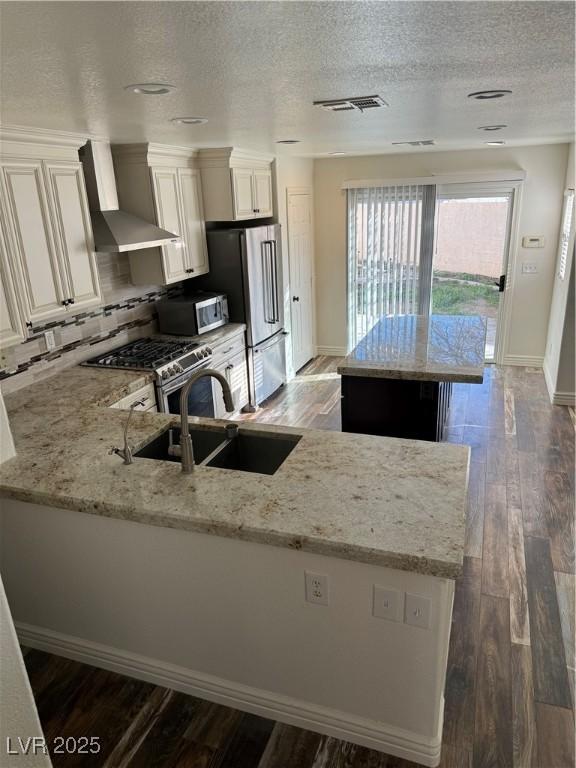 kitchen featuring dark wood finished floors, high quality appliances, light stone counters, wall chimney range hood, and a sink