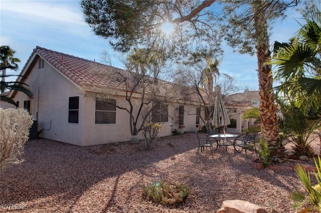 back of house with a tile roof, central AC unit, and stucco siding