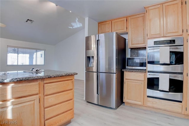 kitchen with light wood finished floors, dark stone countertops, vaulted ceiling, stainless steel appliances, and light brown cabinets