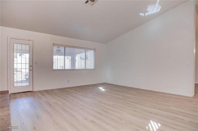 unfurnished room with lofted ceiling, light wood-type flooring, visible vents, and baseboards