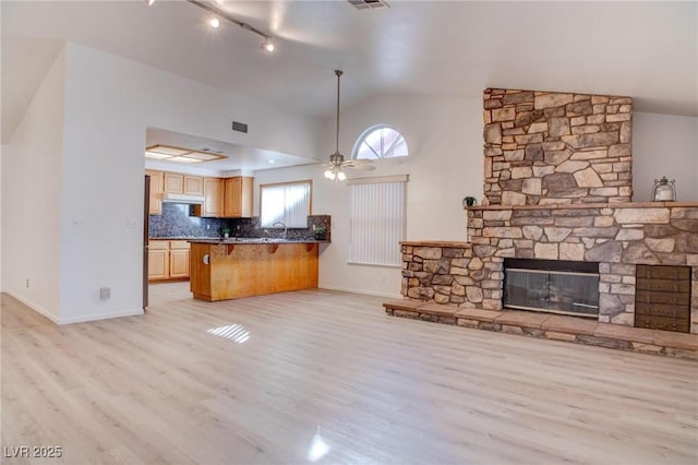 kitchen with tasteful backsplash, a ceiling fan, open floor plan, a stone fireplace, and light wood-type flooring