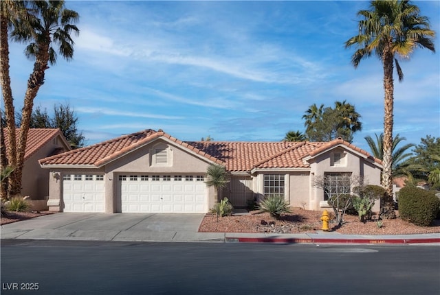 mediterranean / spanish-style house featuring an attached garage, a tile roof, concrete driveway, and stucco siding