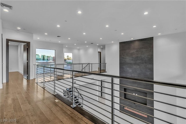 hallway with an upstairs landing, visible vents, wood finished floors, and recessed lighting