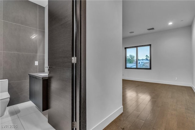 bathroom featuring baseboards, visible vents, toilet, wood finished floors, and vanity