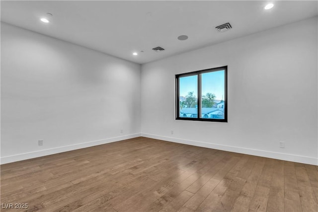 spare room with baseboards, visible vents, and wood finished floors