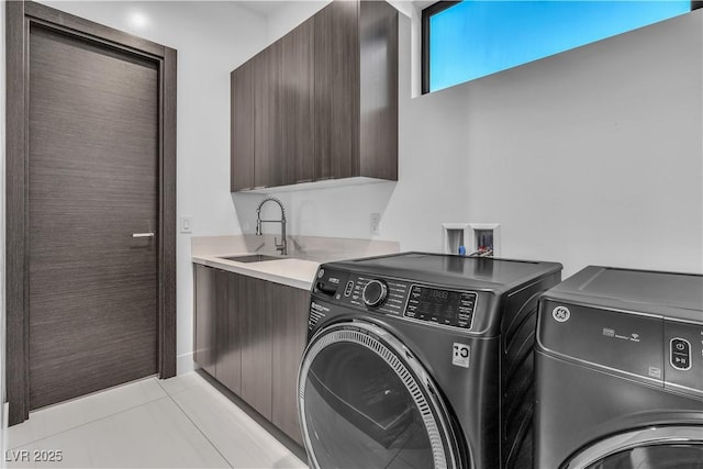 washroom with light tile patterned floors, washer and clothes dryer, a sink, and cabinet space