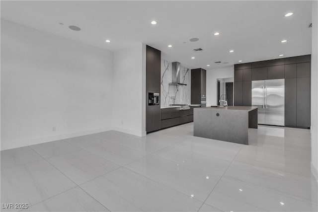 kitchen with stainless steel built in refrigerator, an island with sink, wall chimney exhaust hood, and modern cabinets