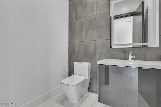 bathroom featuring baseboards, toilet, tile patterned floors, a sink, and tile walls