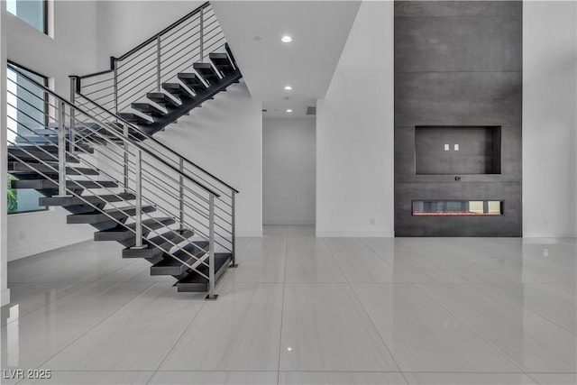 staircase featuring recessed lighting, baseboards, a fireplace, and a high ceiling