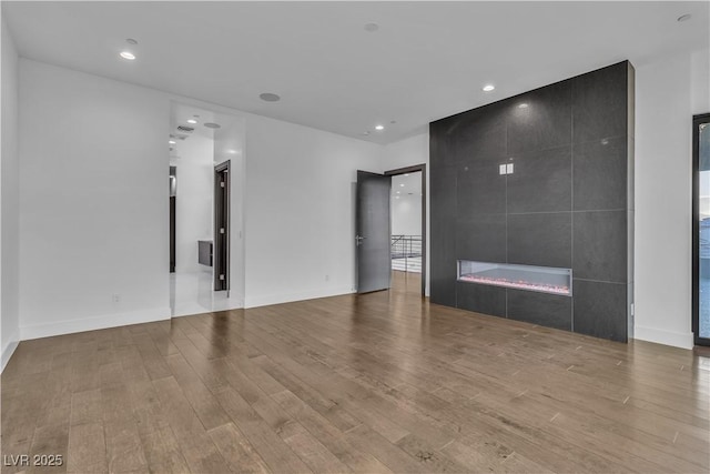 unfurnished room featuring baseboards, a fireplace, wood finished floors, and recessed lighting