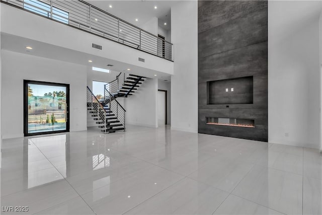 unfurnished living room with stairway, a large fireplace, visible vents, and a towering ceiling