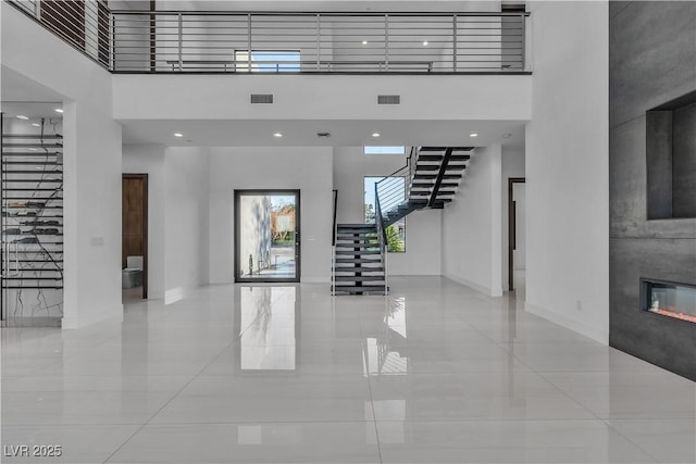 unfurnished living room featuring stairs, a high ceiling, and a glass covered fireplace