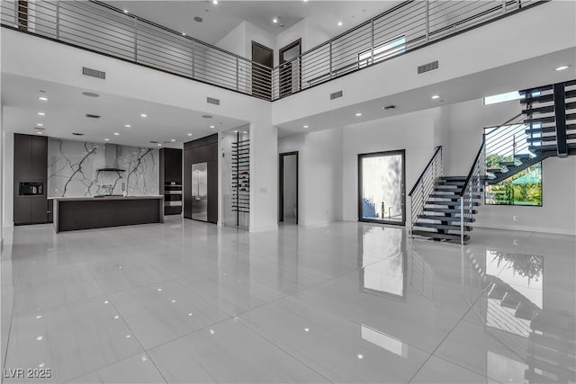 unfurnished living room with stairway, a towering ceiling, and visible vents