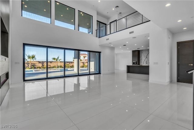 unfurnished living room featuring recessed lighting, visible vents, a towering ceiling, and baseboards