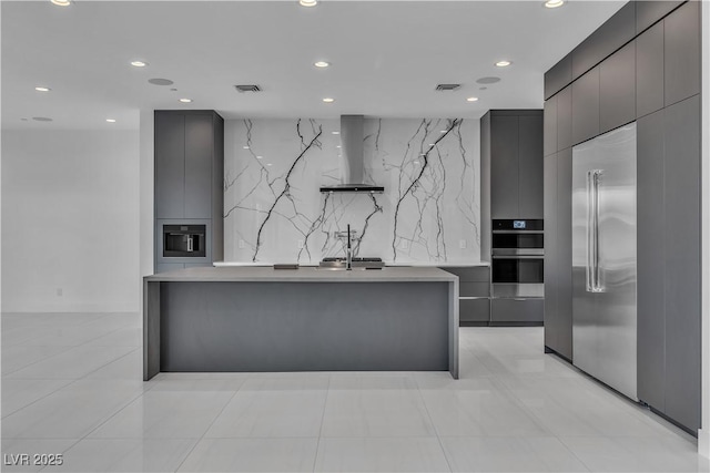 kitchen featuring stainless steel appliances, wall chimney exhaust hood, modern cabinets, and an island with sink