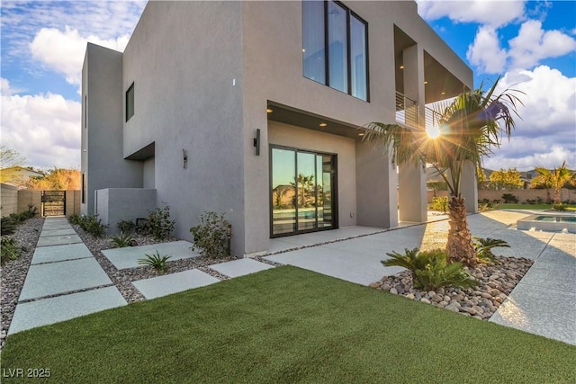 rear view of property featuring a patio, a balcony, a gate, a yard, and stucco siding