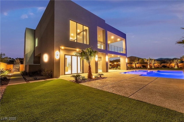 back of property at dusk with a lawn, a patio area, a balcony, an in ground hot tub, and an outdoor pool