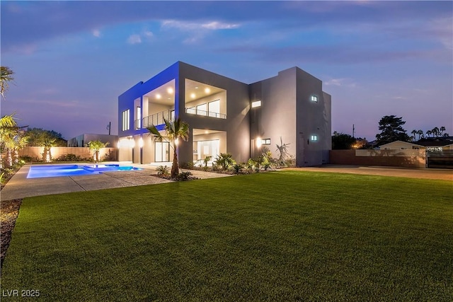 back of house at dusk featuring a fenced in pool, a balcony, fence, a yard, and stucco siding